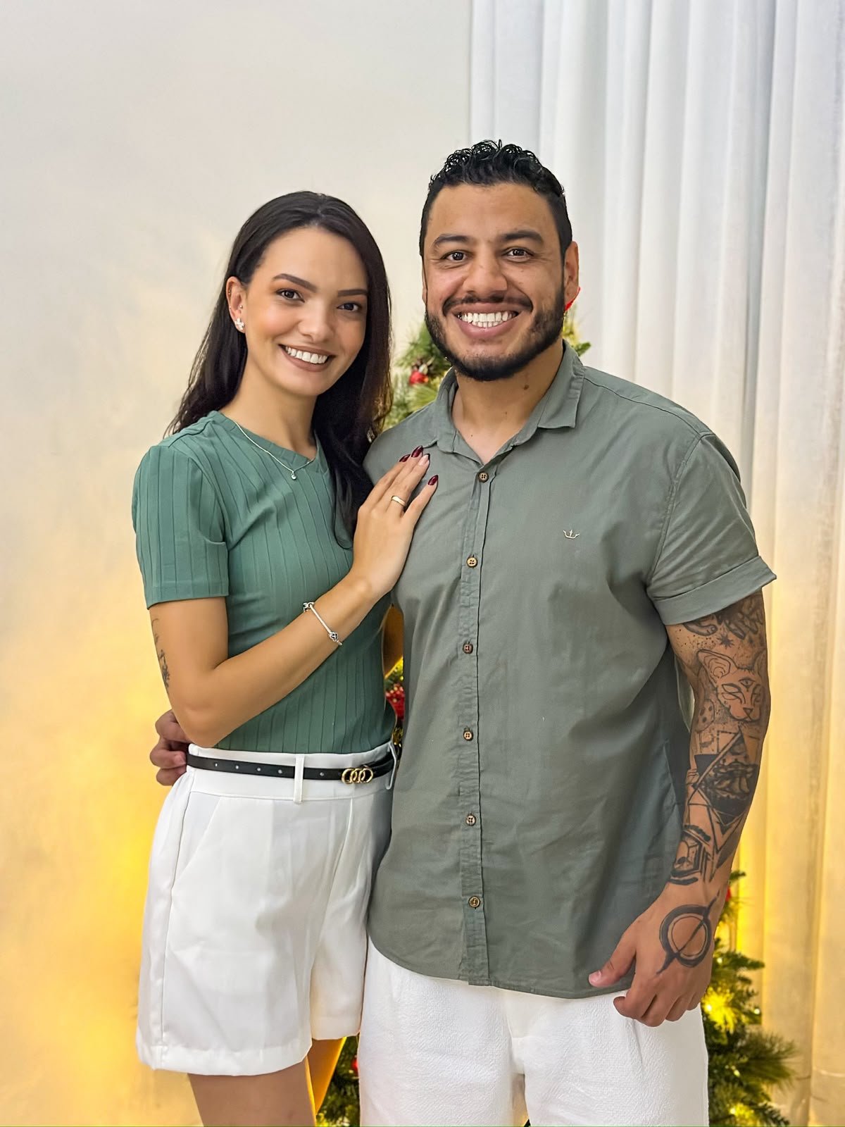 Retrato de Cássia e Pablo sorrindo, em ambiente interno decorado para o Natal